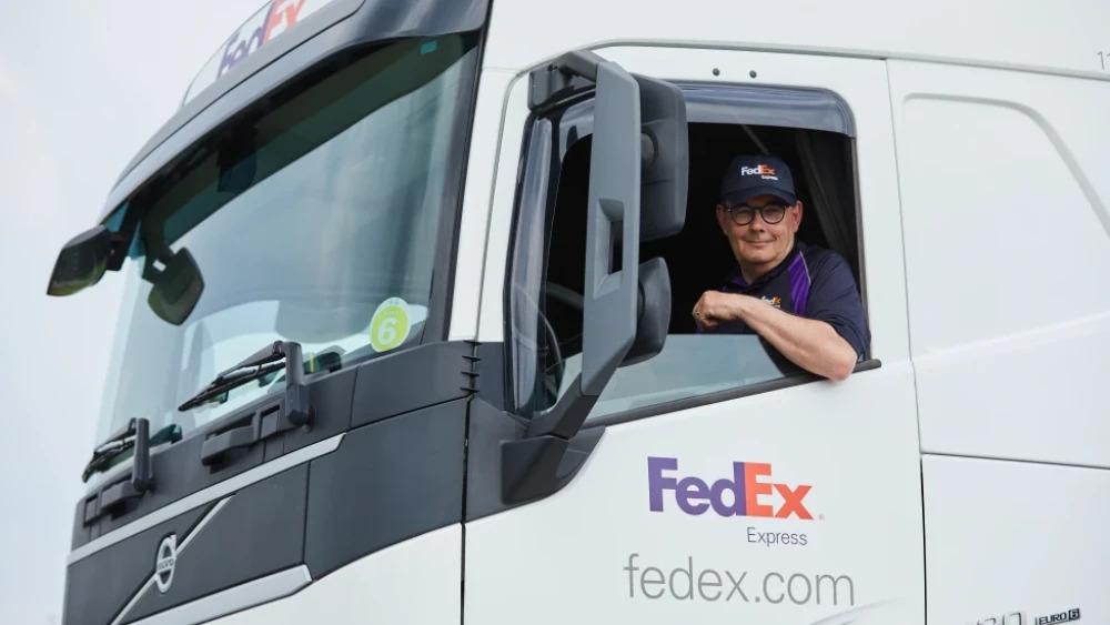 An employee leaning out of the window of a FedEx truck.