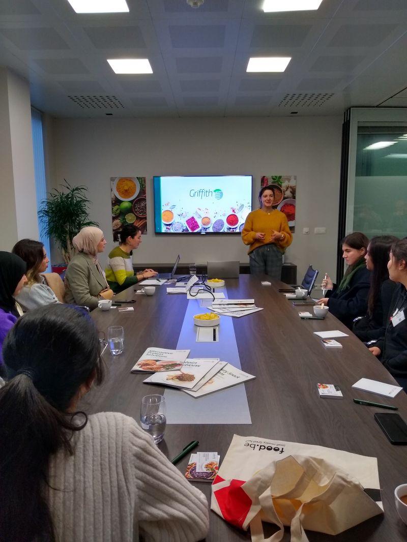 A person presenting to a conference room of others seated.