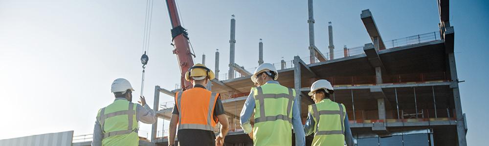 Four construction workers stood in a line looking at a building being built