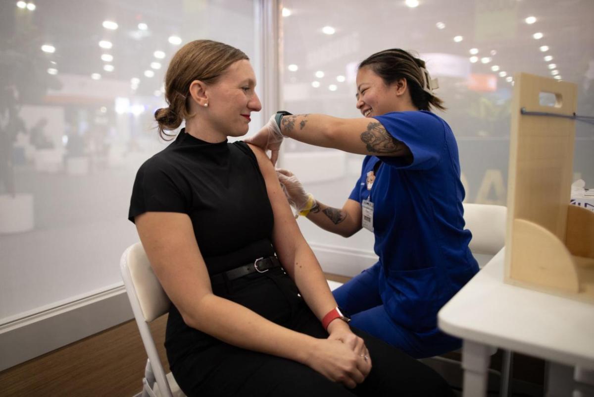 A person receiving a vaccination from a person in blue scrubs.