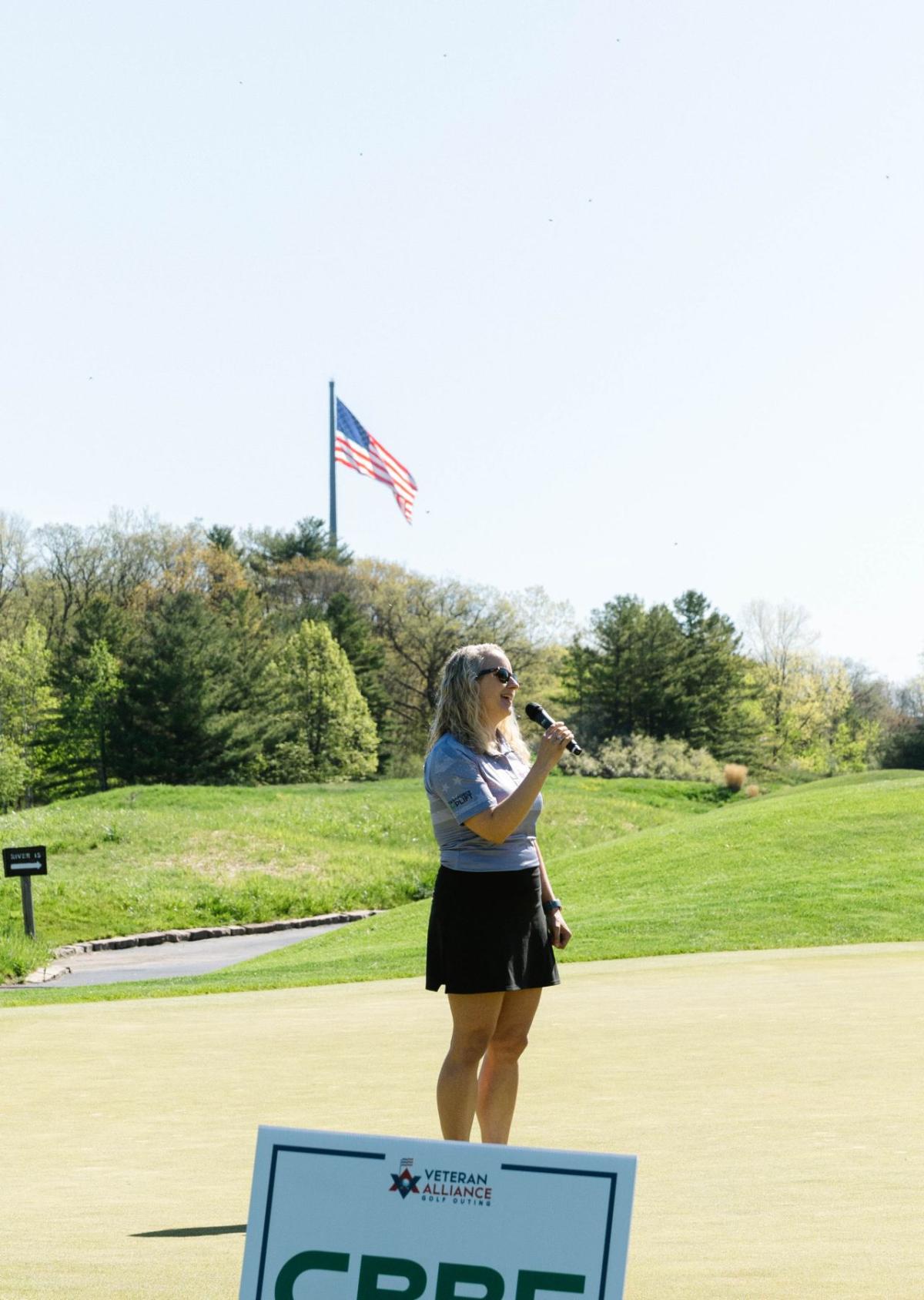 A person standing on a golf course holding a microphone.