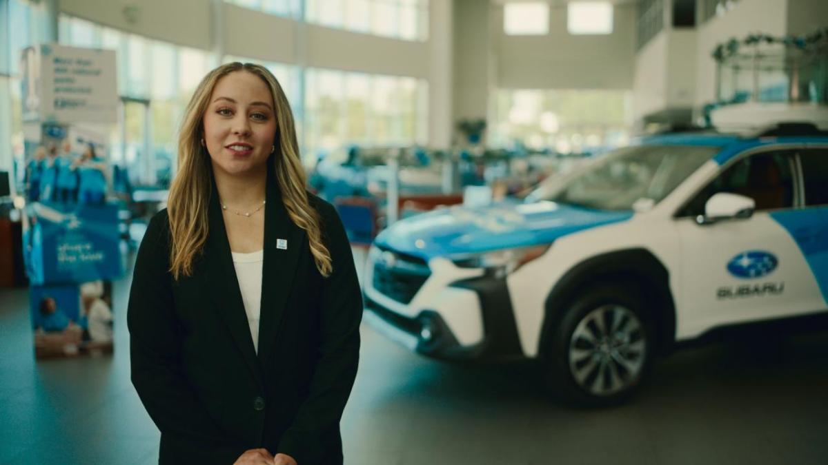 A person standing next to a car in a Subaru dealership