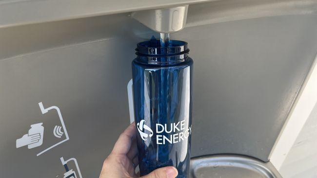 A reusable water bottle being refilled at a water station.