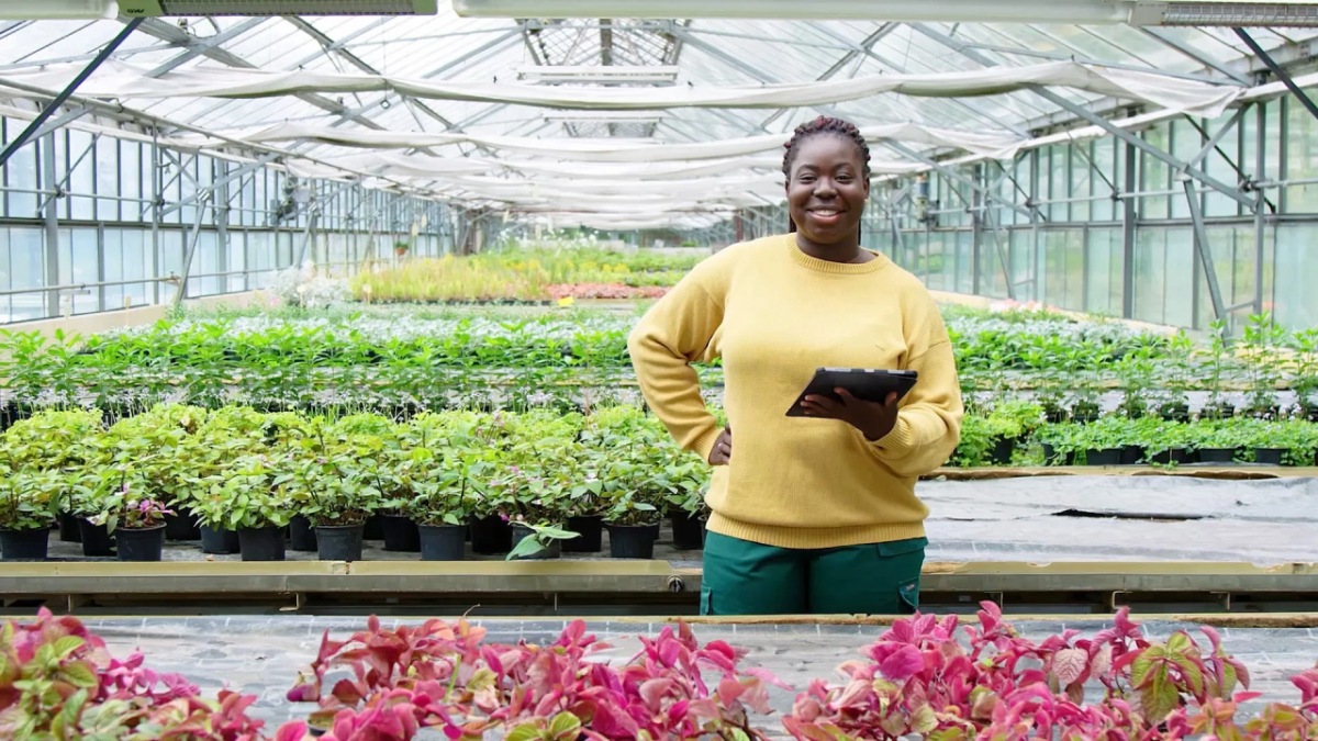 A person holding a tablet and smiling inside a greenhouse