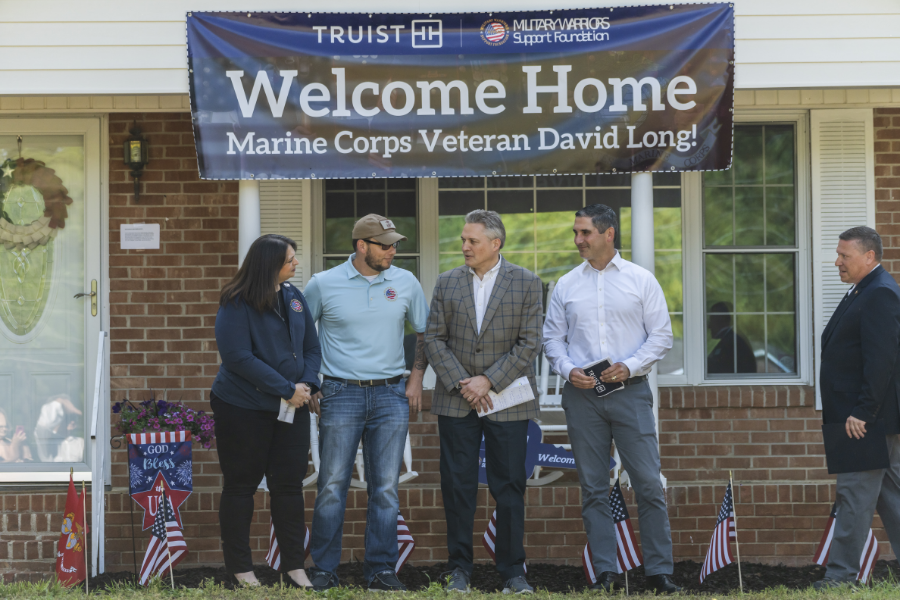 Sgt. David Long and three others stand outside his new home, a banner above them "Welcome Home"