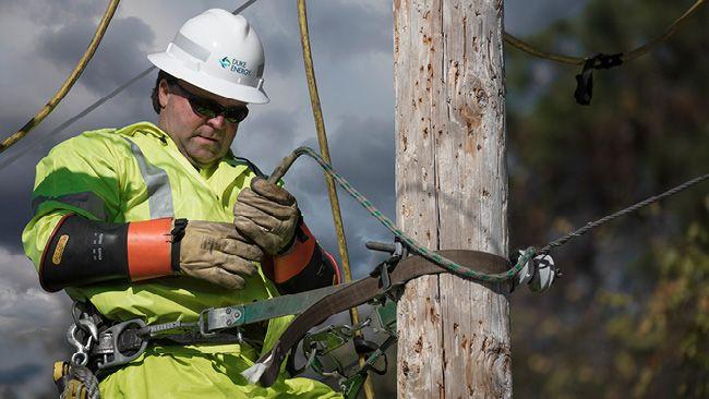 A repair person high on an electrical pole, holding a wire. 