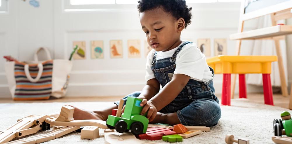 A child seated on on the floor playing with wooden toys.